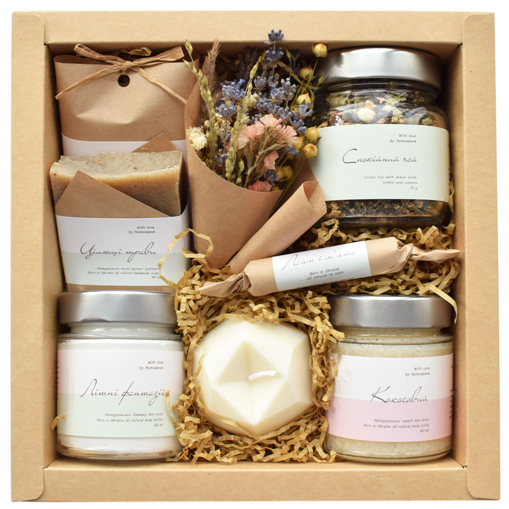 Kraft gift box tied with twine and ribbon, holding wrapped soaps, a candle and cotton